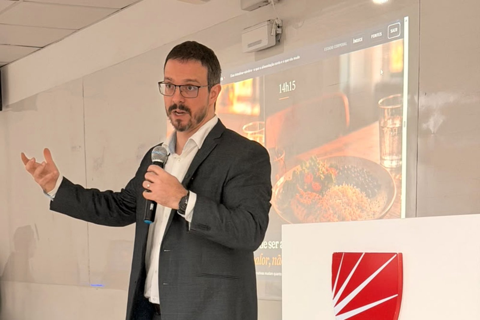 Dr. Guilherme Loureiro Fracasso falando ao microfone durante apresentação na 3ª Jornada da Alimentas, com slide sobre o eixo intestino-cérebro projetado ao fundo. Dr. Guilherme Loureiro Fracasso, Médico Psiquiatra, CRM-RS 36.500 | RQE 32.771.